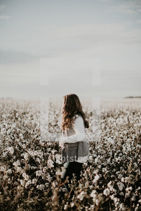a woman walking through a field of cotton 