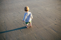 toddler boy standing on sand on a beach 