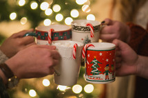Four Christmas cups with hot cocoa and candy canes are put together to make a toast.