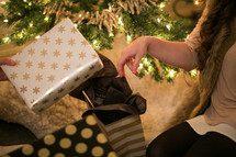 Women sitting near a Christmas tree with wrapped gifts.