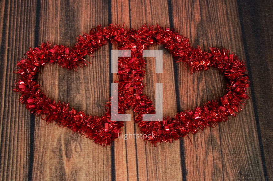 Two hearts made of red tinsel on wooden boards.