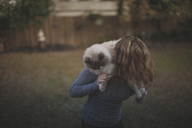 A blonde girl holding her cat behind her head