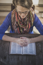 A woman sitting at a table praying with an open Bible