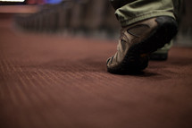 feet of a man walking down the aisle of a church 