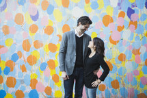 a man and a woman standing in front of a colorful wall 