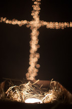 bokeh Christmas lights in the shape of a cross over a glowing manger