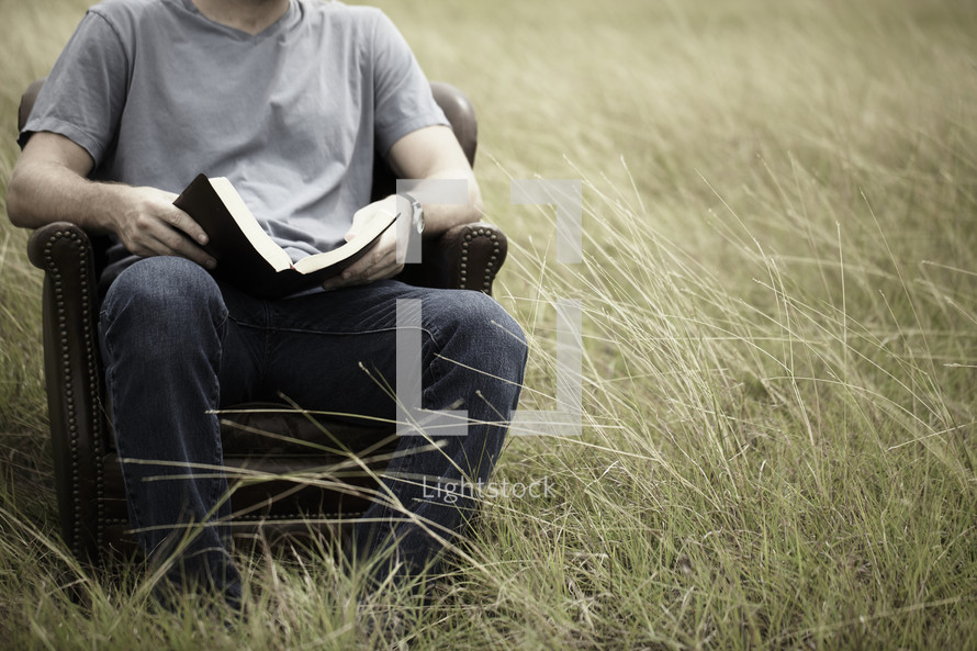 A young man studies the Bible in a grassy field.