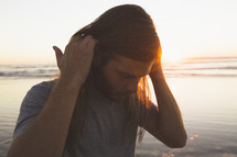 a man tucking his long hair behind his ears on a beach 