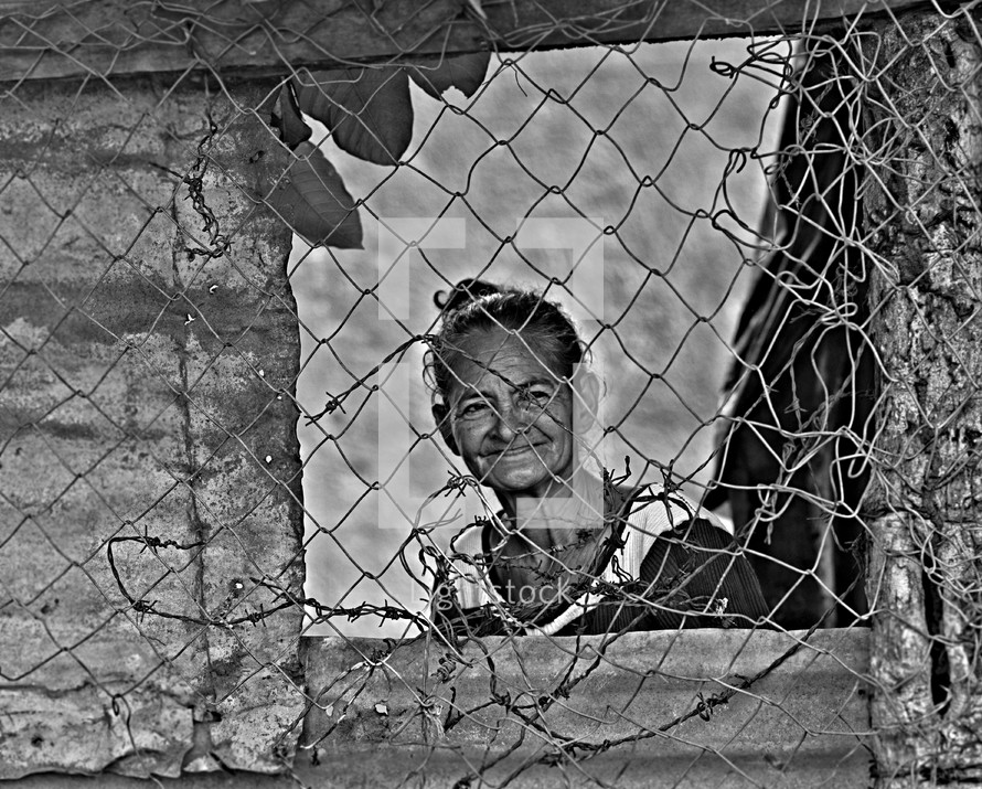 face of an elderly woman behind a chain link fence 