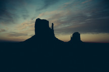 Silhouettes of steep buttes at dusk.