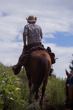 a man wearing a cowboy hat riding a horse on a mountain trail 