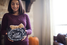 a woman in a sweater holding a give thanks plaque 