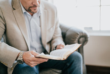 man in a suit sitting reading a Bible 