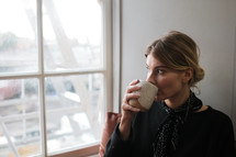 a woman drinking coffee by a window 