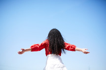 back of a woman with outstretched arms looking up