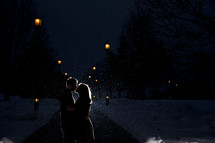 Silhouette of a couple kissing in the snowfall at night.