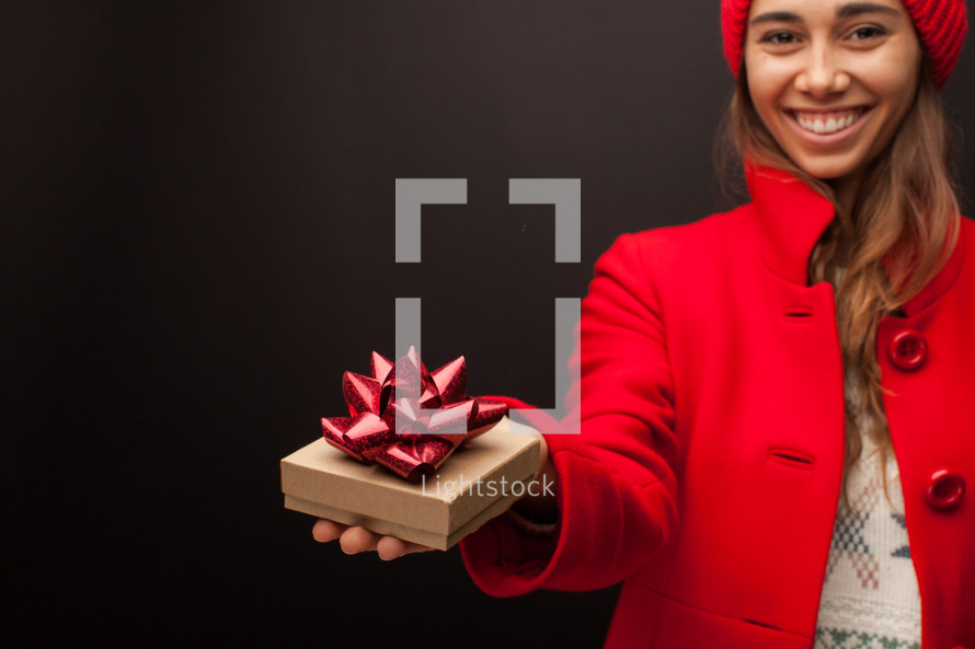 a woman in a red peacoat holding a gift box for Christmas 
