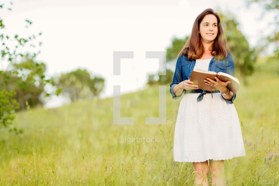 woman standing in a field reading a Bible