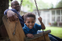 A father and son sitting in a swing in the back yard.