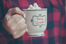 a man in a plaid shirt holding a mug of hot cocoa 