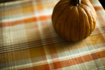 a pumpkin on a plaid table cloth 