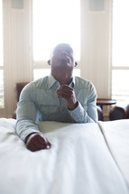 a man in prayer kneeling at the side of a bed 