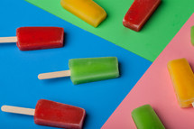 Brightly colored popsicles arranged on different colored papers.