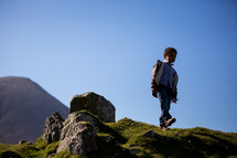 a boy walking down a green mountain 