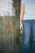 Teen holding a spade shovel near a half painted fence.