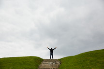a man standing at the top of a hill with arms raised 