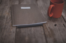 A pen and notebook next to an orange coffee mug