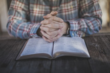 A man with hands folded in prayer on an open Bible
