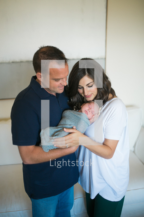 mother and father holding a swaddled newborn baby 
