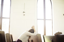 a woman praying sitting in a church pew 