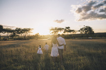 a family walking through tall grass at sunset 