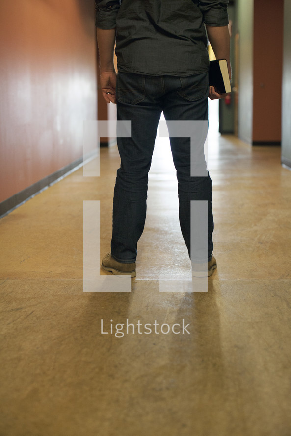 man standing in a hallway holding a Bible 