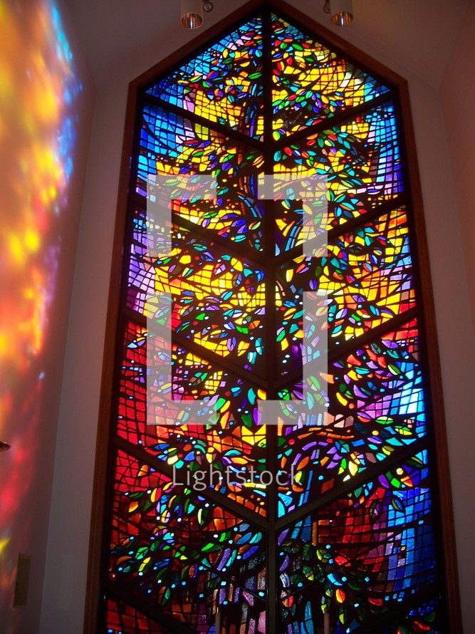 A stained glass window reflects light on the walls of the church providing a warm glow of light and a prism of colors showing the light and love of Heaven.