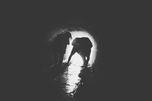 Silhouette of a couple walking through a wet drainage pipe.