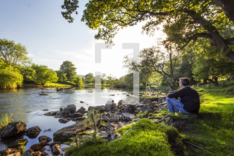 a man sitting on a river bank watching the water 