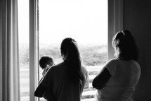 grandmother, mother, and daughter looking out a window at the rain 