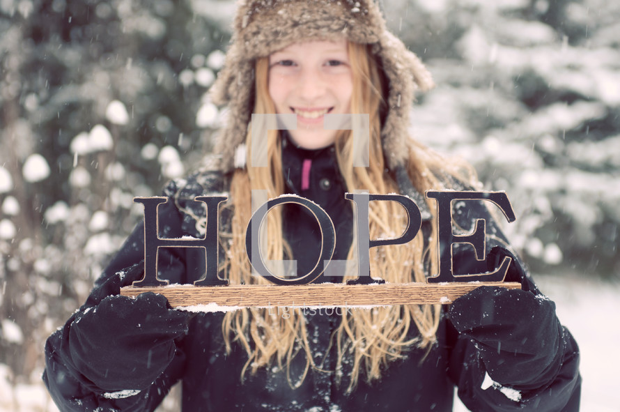 A girl in winter clothes holding a sign that says, "Hope,"