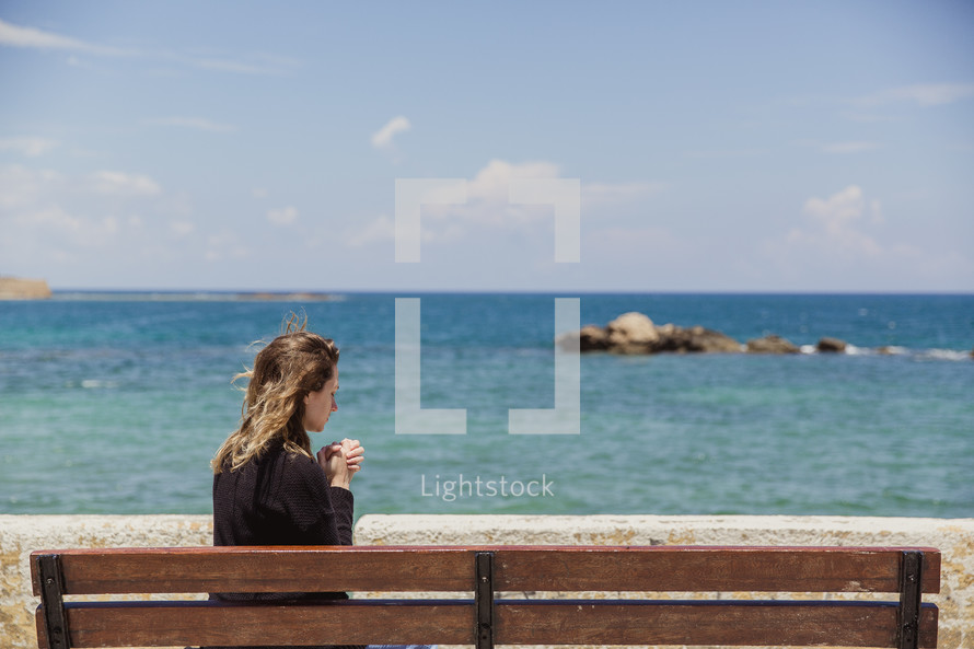 woman in prayer sitting on a bench at a beach in Greece