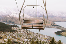An empty ski lift chair in the air above a town.