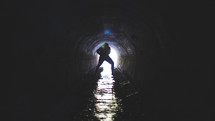 Silhouette of a man in a wet drainage pipe.