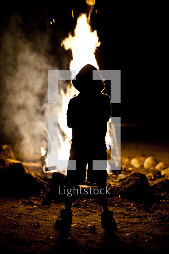 The silhouette of a hooded child standing in front of a fire