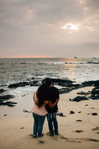 a couple standing on a beach hugging at sunset 