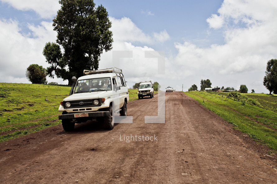 White sports utility vehicles travel down a remote dirt road.