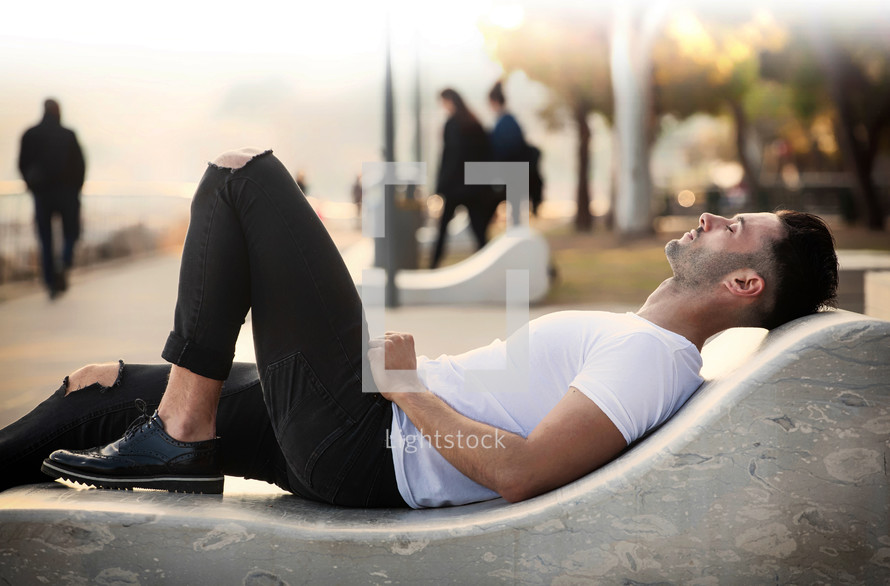 young man lying near the sea on a bench in relaxation