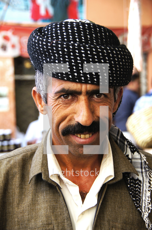 Kurdish Man with moustache and beret with busy market place in background. [For more like this search Ethnic face]