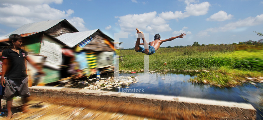 A young boy jumps and dives into a flooded river.